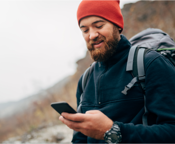 young man hiking. He is wearing a red tuque and holding a phone